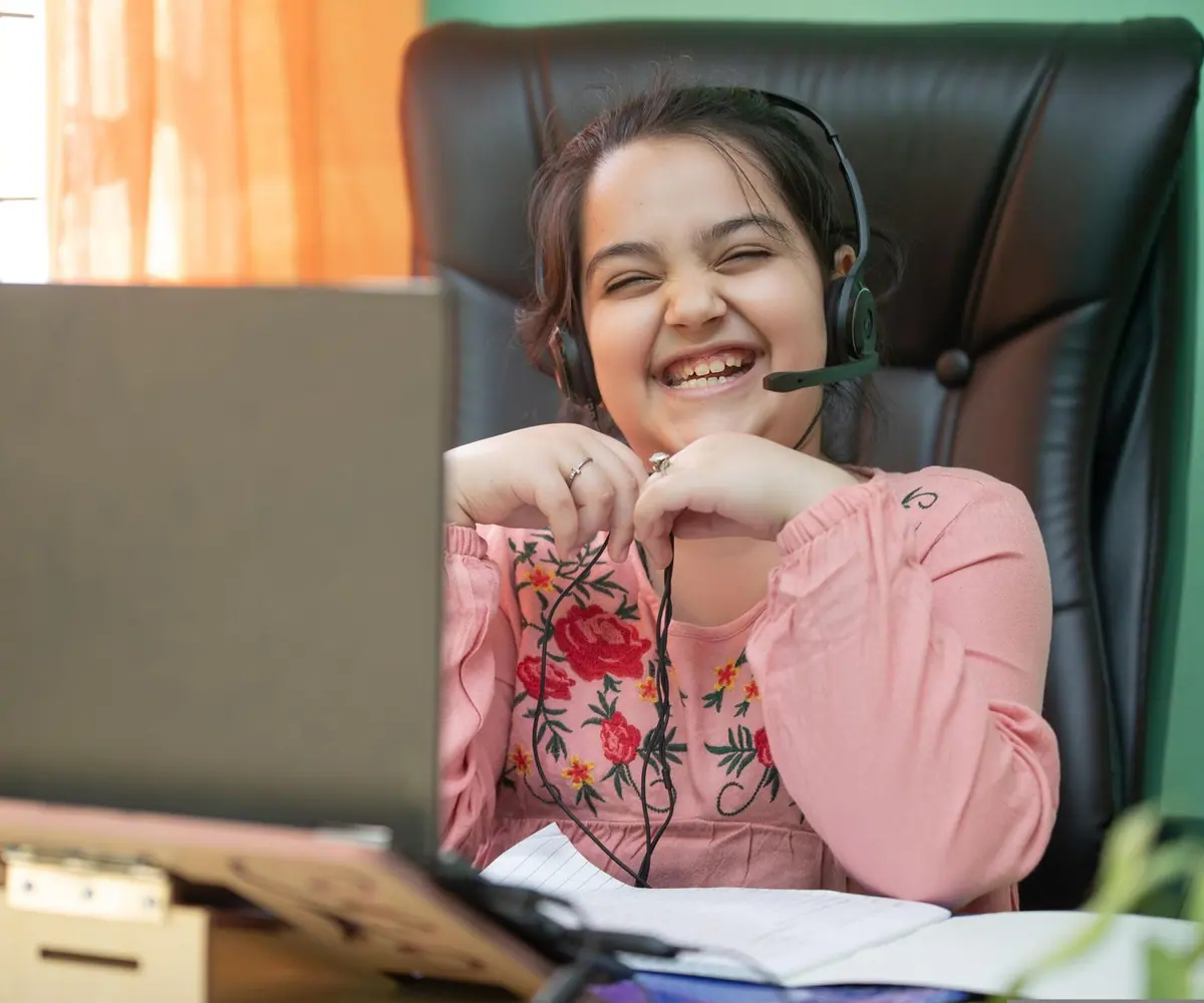 A smiling student wearing a headset during an online lesson on a laptop at home