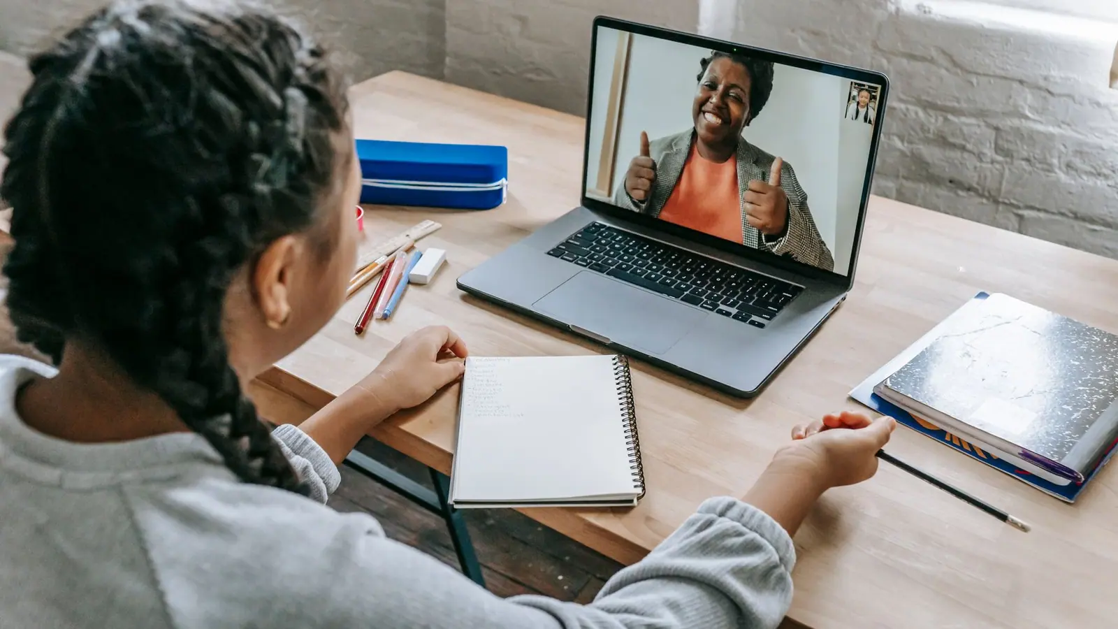 A student studying at home on a video call with a tutor on a laptop