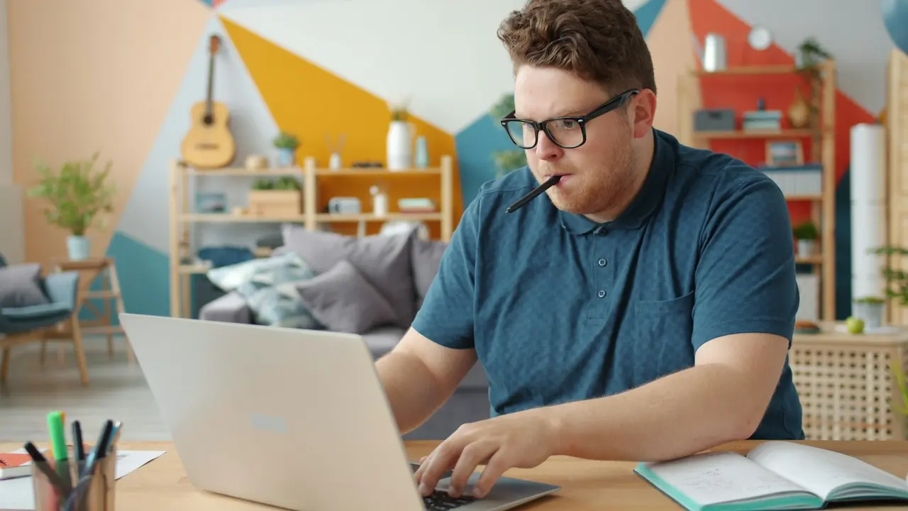 A person working at a laptop with a notebook open on a desk in a bright home
