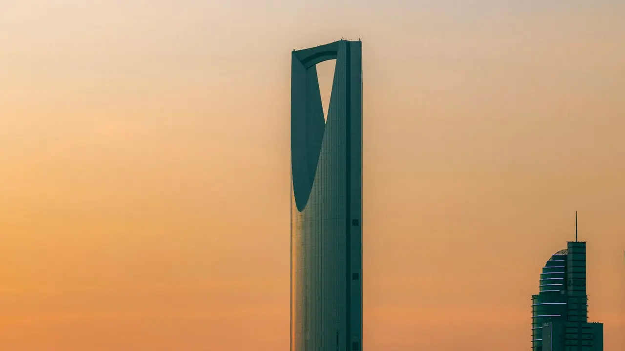 The Kingdom Centre tower in Riyadh against a warm orange sky at dusk