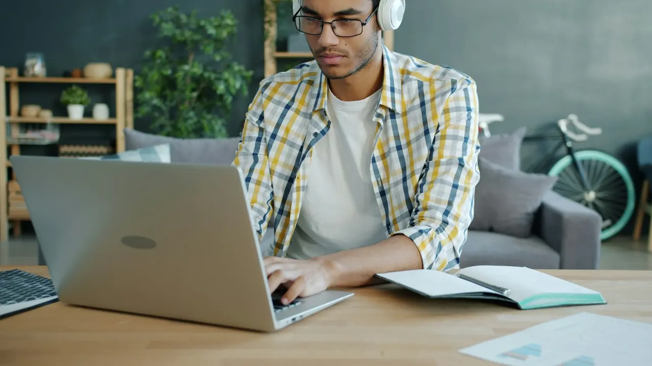 A student wearing headphones studying online with a laptop and notebook at a desk