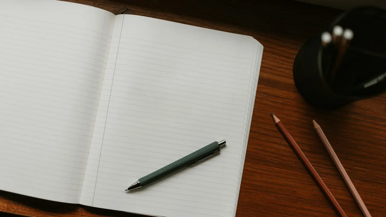 An open lined notebook with a pen and two pencils on a wooden desk, ready for a study session